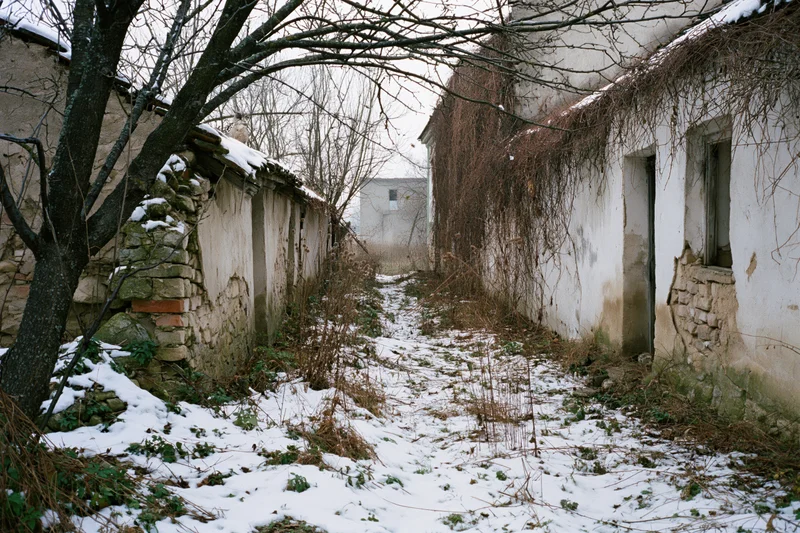 Narrow snow-covered alley between crumbling stone walls in an abandoned village