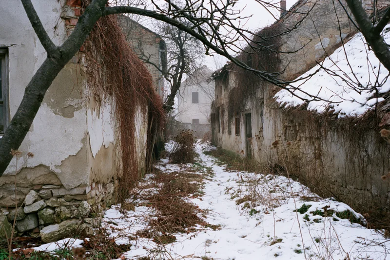 Narrow snow-covered alley between crumbling derelict buildings in abandoned village