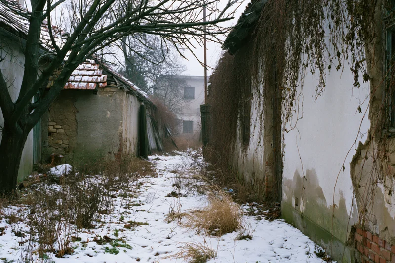 Narrow snow-covered alley between crumbling derelict buildings in a rural village
