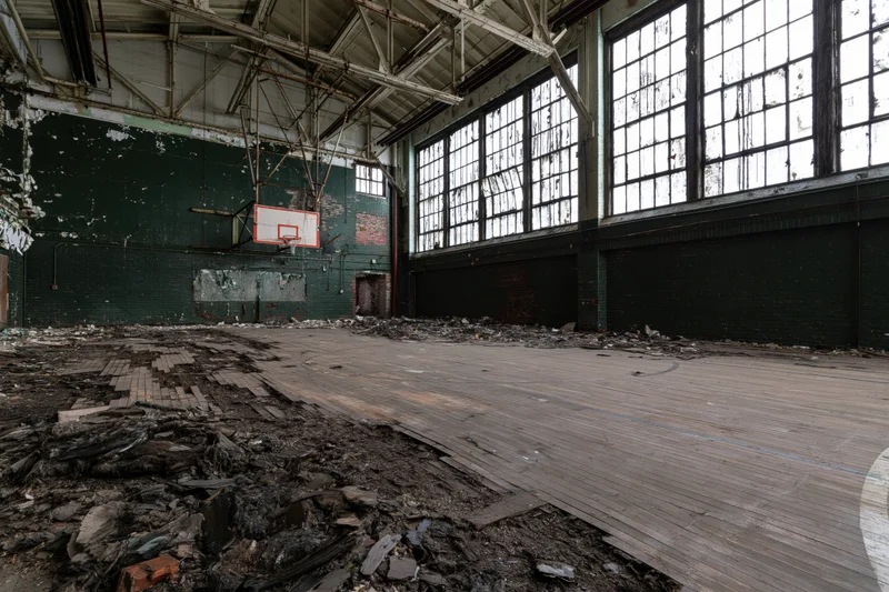 Abandoned school gymnasium interior with decaying basketball court and debris on wooden floor