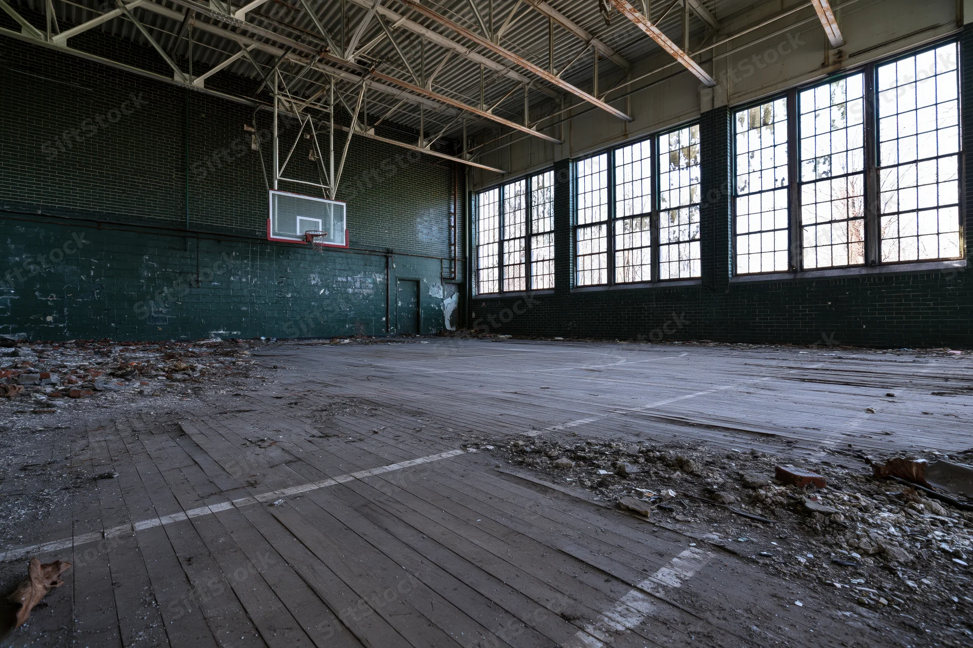 Abandoned school gymnasium interior with decaying wooden floor and broken windows