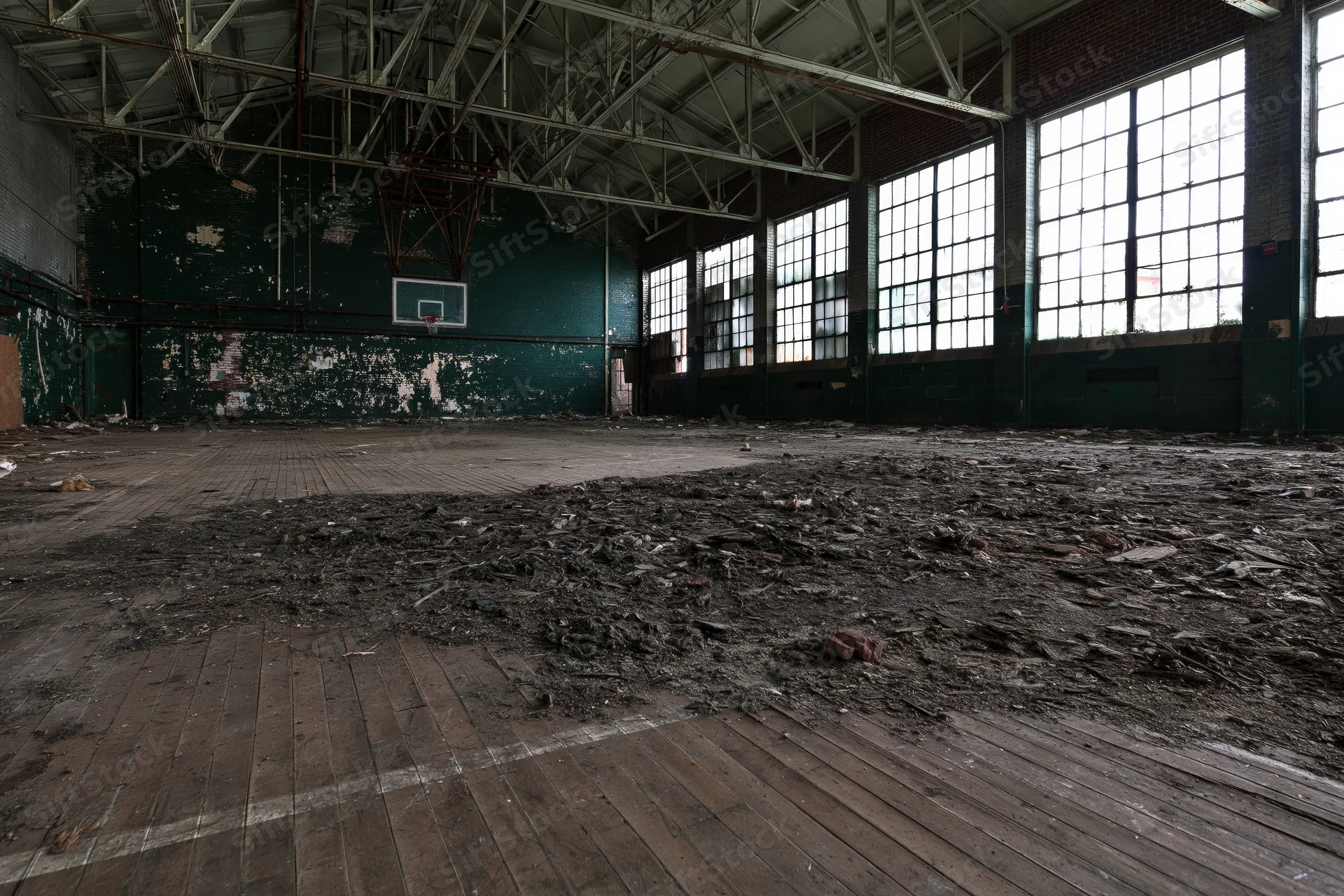 Empty decaying gymnasium interior with peeling paint and debris on wooden floor