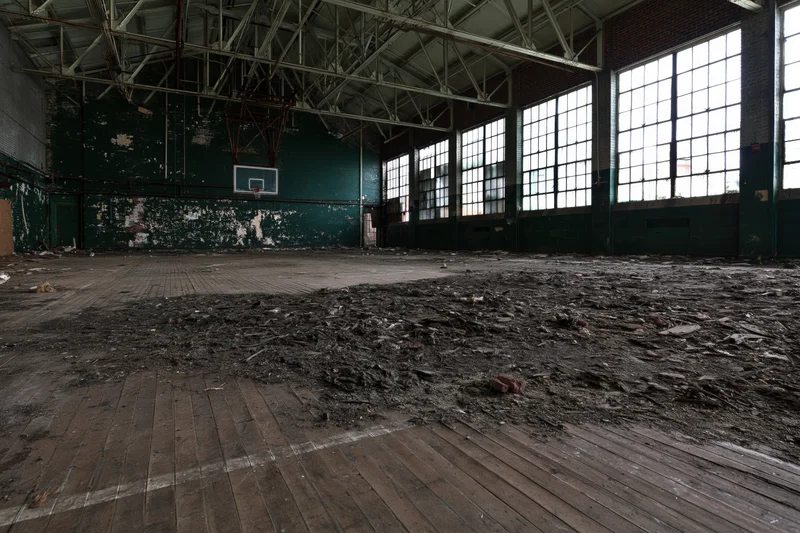 Empty decaying gymnasium interior with peeling paint and debris on wooden floor