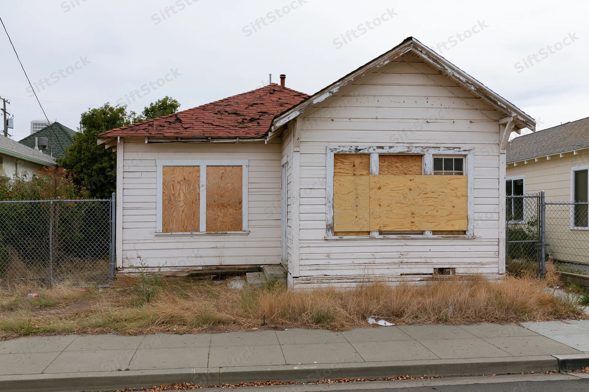 Abandoned single-story clapboard house with boarded-up windows on a residential street