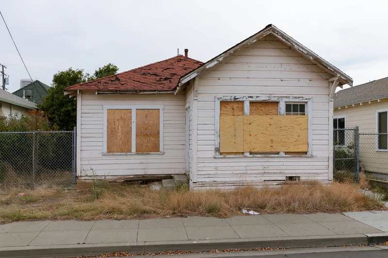 Abandoned single-story clapboard house with boarded-up windows on a residential street