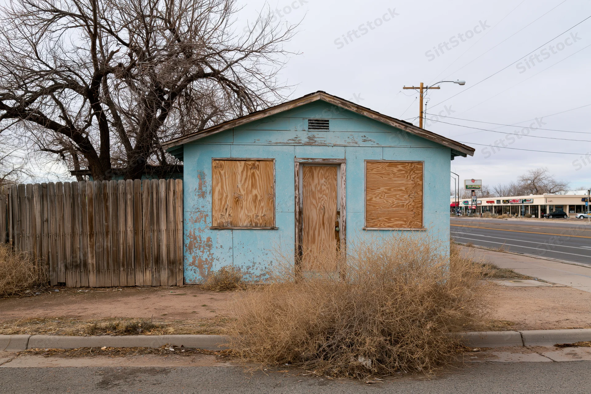 Abandoned single-story house with boarded-up windows and door on a roadside lot