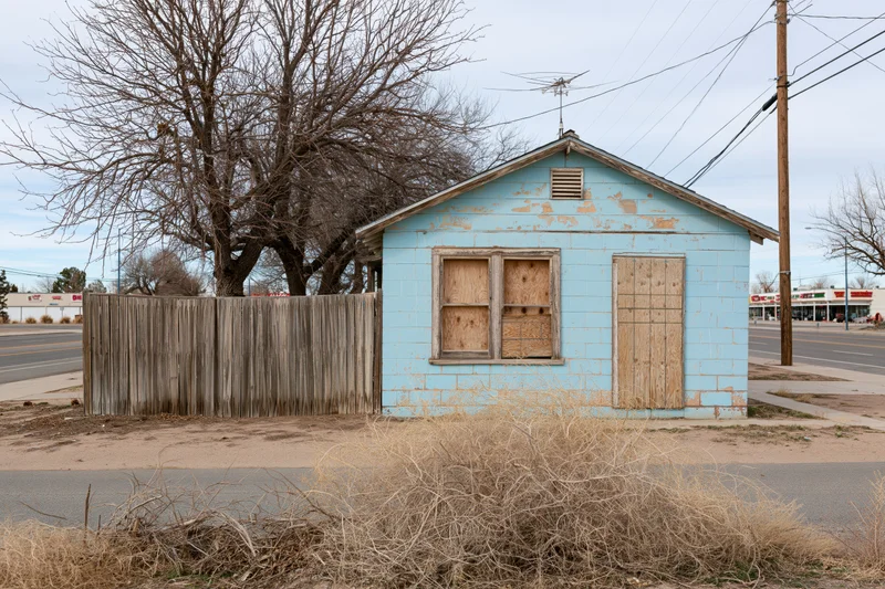 Abandoned single-story house with boarded windows and door on a residential street