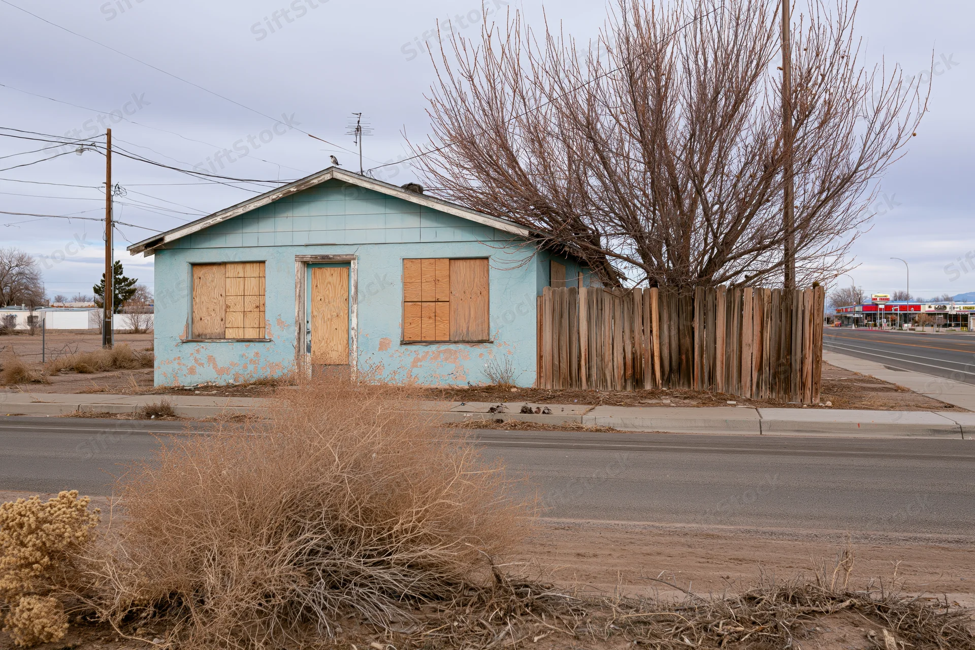 Abandoned single-story house with boarded windows and door along a roadside in a dry rural area