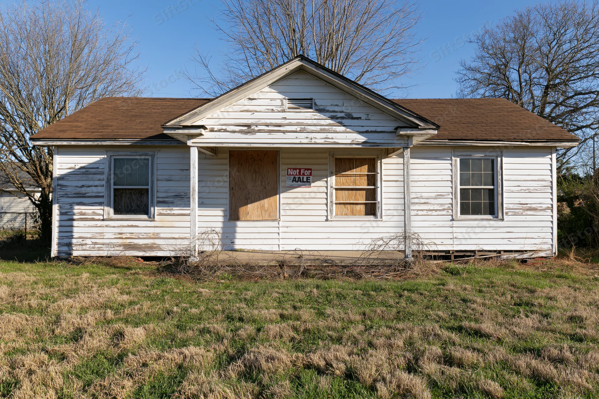 Abandoned single-story ranch house with boarded windows and not for sale sign on front porch in rural yard