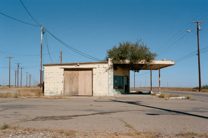 Abandoned single-story roadside service station with boarded door and overhang under clear blue sky