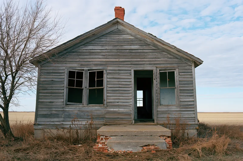 Abandoned wooden farmhouse with open door and broken windows in a rural field