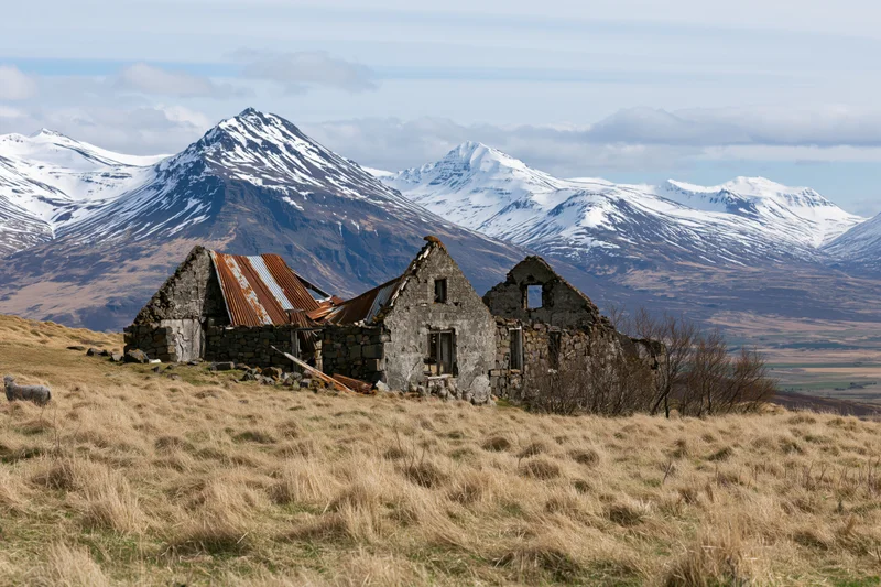 Abandoned stone farmhouse ruins on a grassy hillside with snow-capped mountains in the background