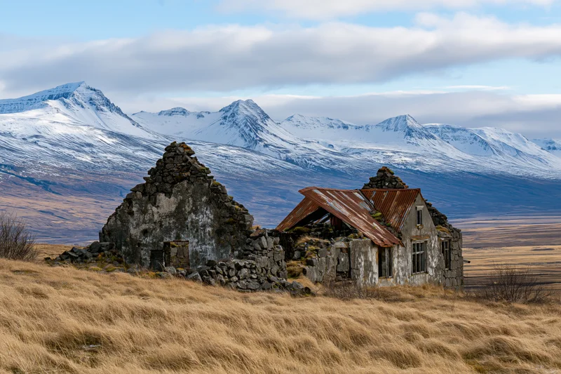 Abandoned stone farmhouse ruins on a grassy hill with snow-covered mountains in the background