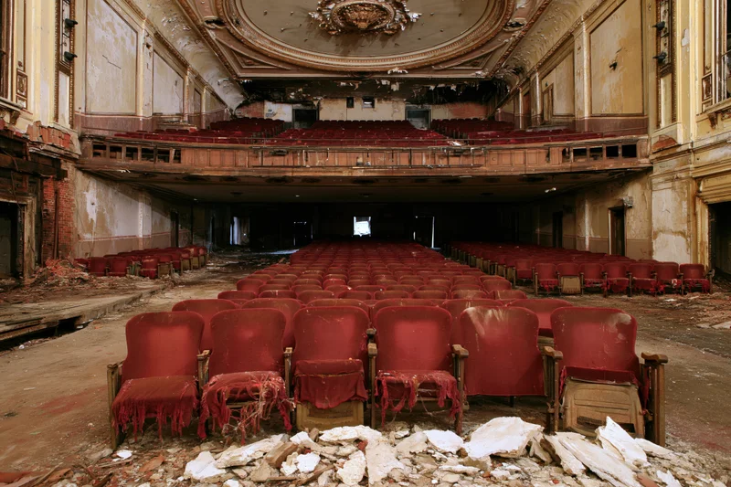 Rows of red seats in a decaying theater interior with broken plaster and exposed brick