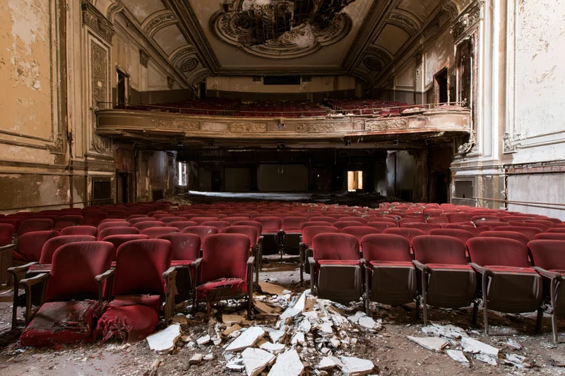 Rows of red seats in a decaying theater interior with rubble on the floor and ornate ceiling details
