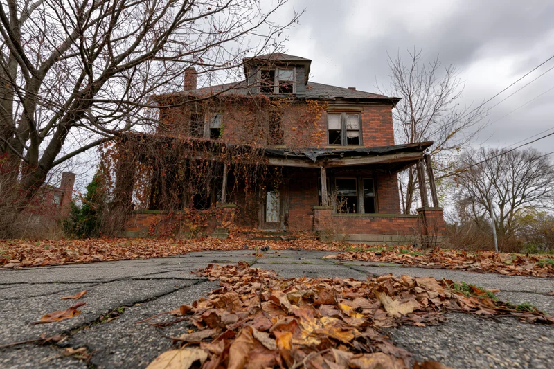 Abandoned two-story brick house with dead vines and fallen leaves on the driveway