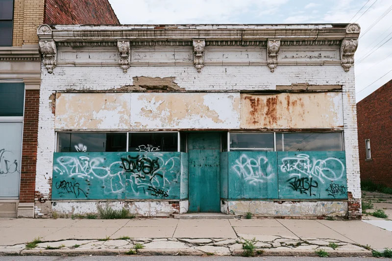 Abandoned two-story storefront with graffiti-covered boarded windows and peeling paint on an urban street