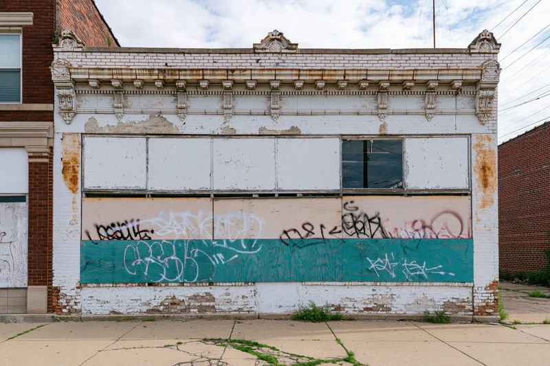 Abandoned two-story storefront with boarded windows and graffiti on a cracked sidewalk