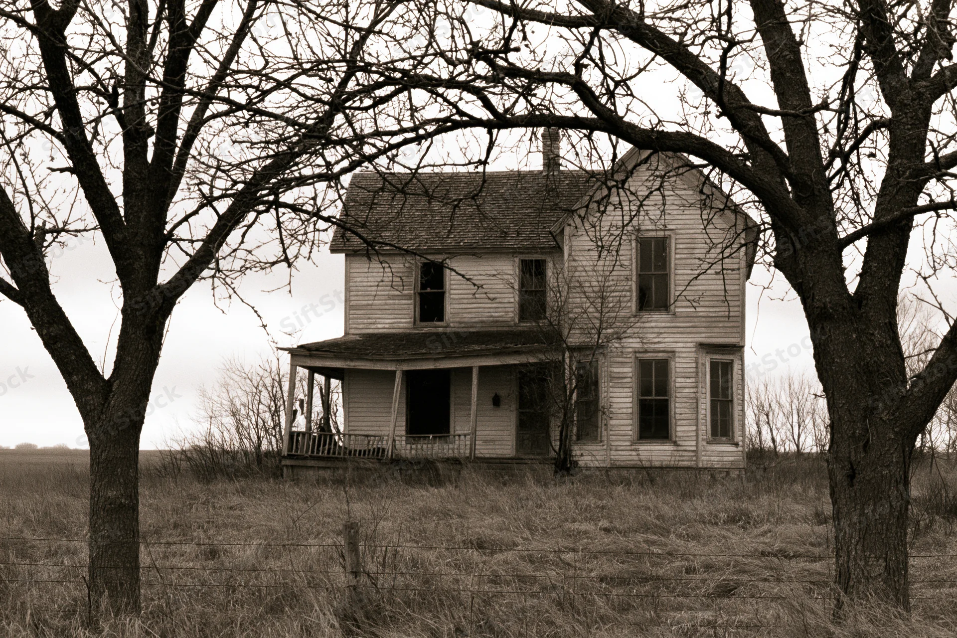 Abandoned two-story wooden farmhouse with sagging porch in a rural field framed by bare trees
