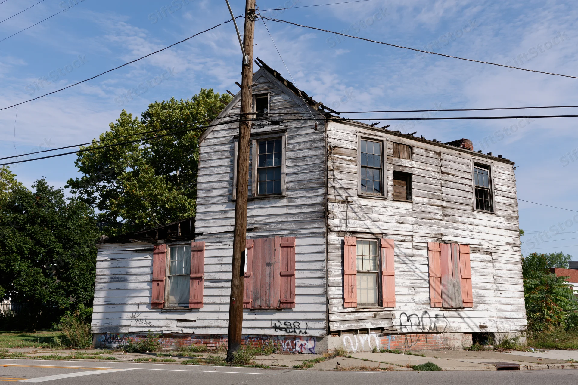 Weathered two-story wooden house with peeling paint and graffiti on a street corner