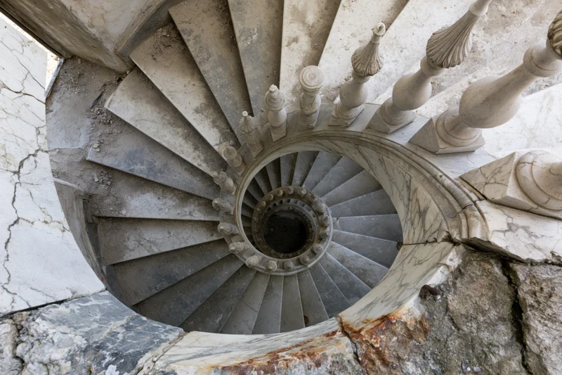 Top-down view of a weathered spiral marble staircase in an abandoned building