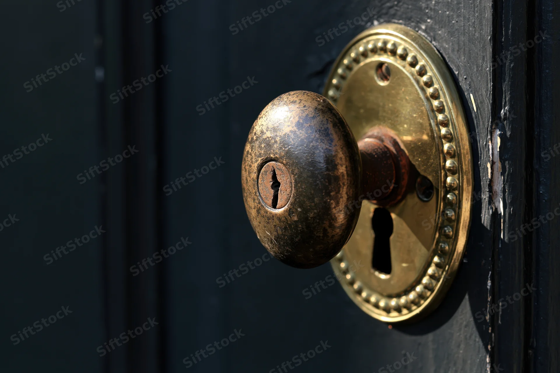 Antique brass door knob with oval beaded escutcheon and keyhole on dark wooden door