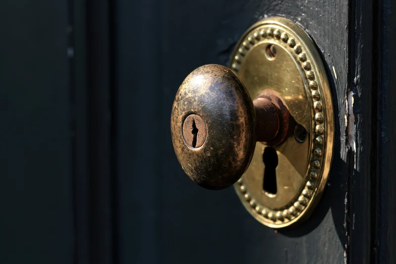 Antique brass door knob with oval beaded escutcheon and keyhole on dark wooden door