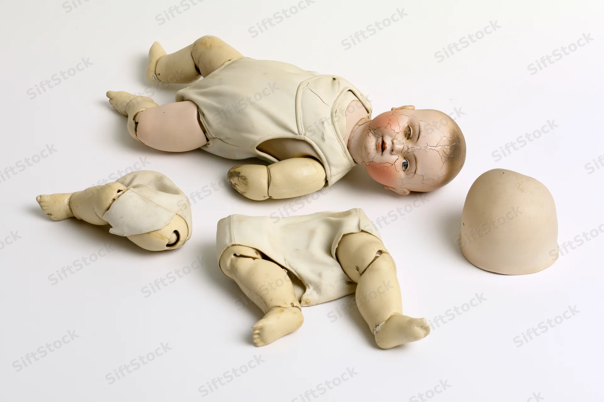 Disassembled antique porcelain baby doll with cracked head and separate limbs on white background
