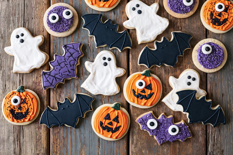 Assorted halloween sugar cookies decorated with royal icing in pumpkin ghost and bat shapes on wooden surface