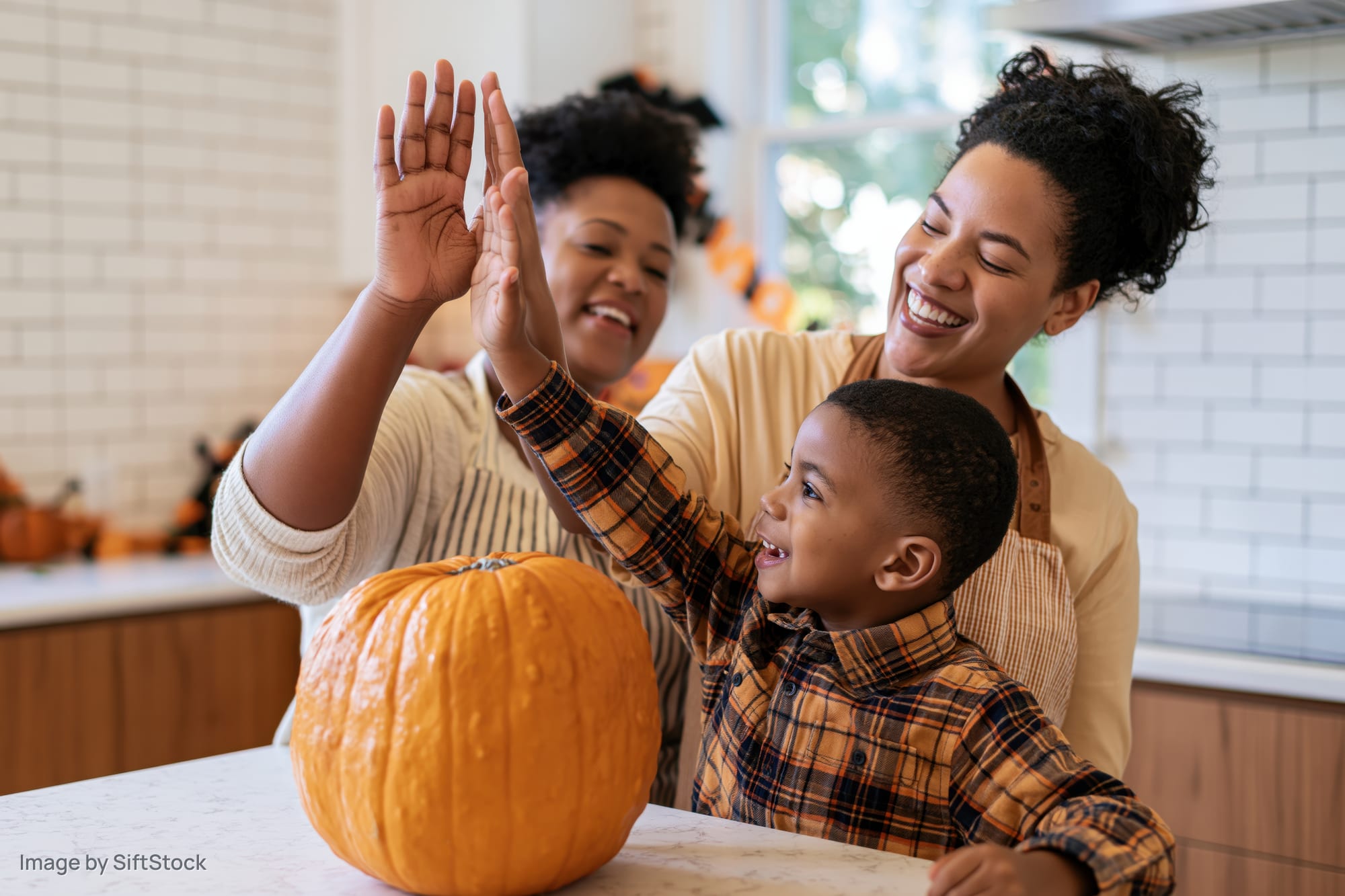 Black mother and young son giving each other a high five over a pumpkin in the kitchen