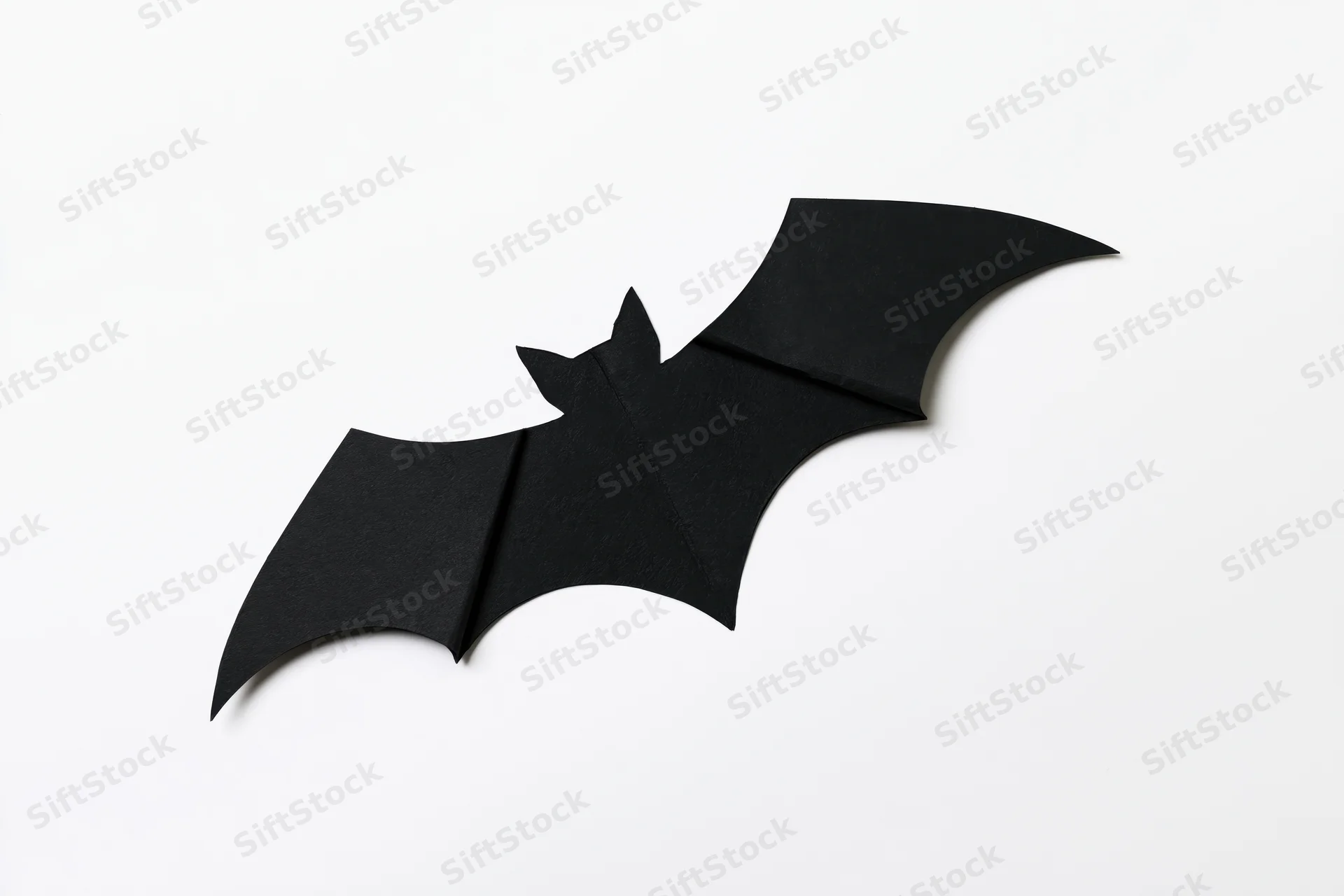 Black paper bat cutout with folded wings isolated on white background