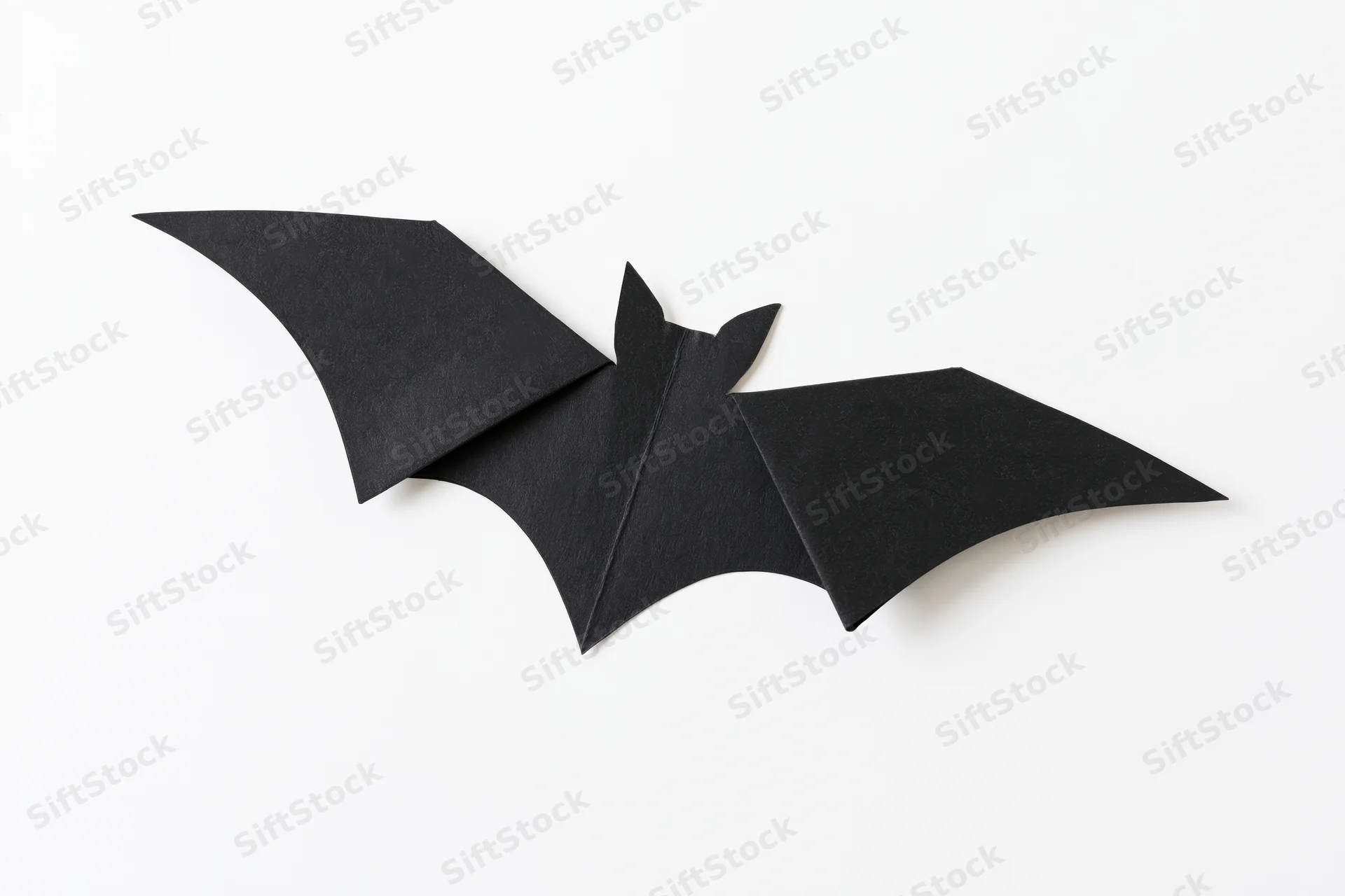 Black paper bat cutout with folded wings isolated on white background