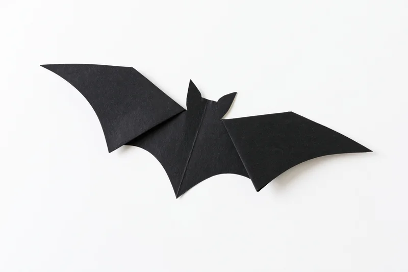 Black paper bat cutout with folded wings isolated on white background