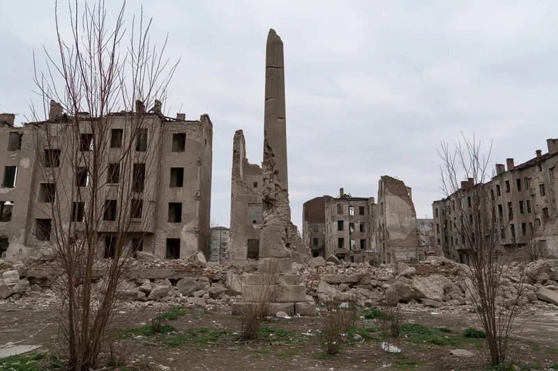 Bombed-out city block with crumbling concrete buildings and rubble under overcast sky
