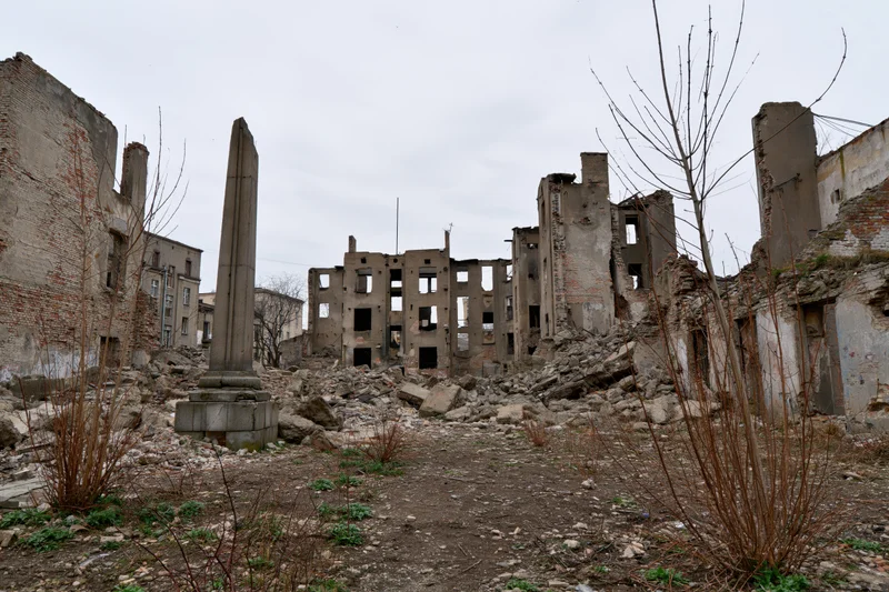 Bombed-out city block with crumbling concrete ruins and scattered rubble under overcast sky