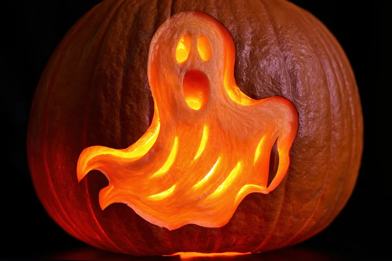 Carved pumpkin with ghost design glowing in the dark
