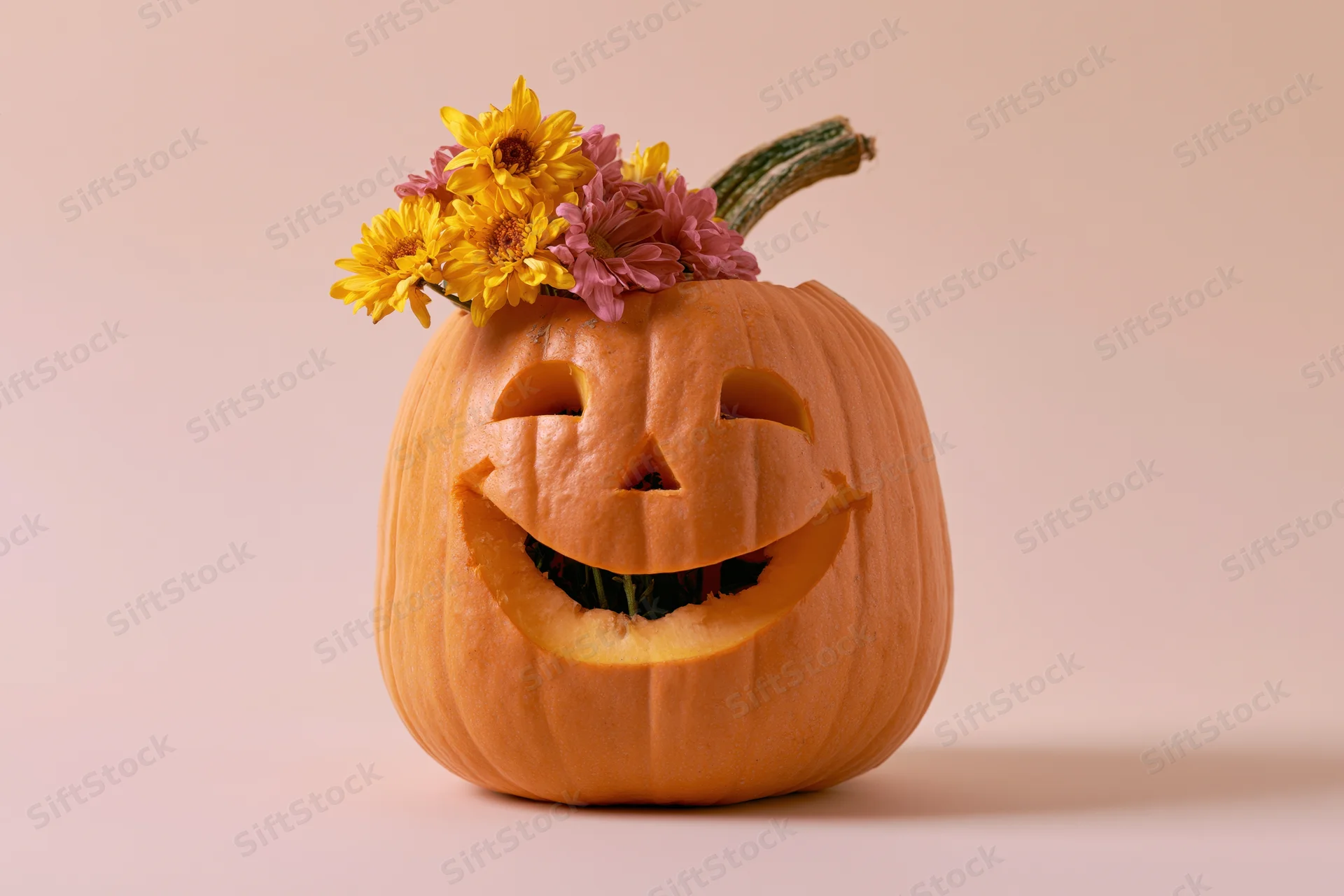Carved pumpkin with a wide friendly smile and flowers on top against a plain background