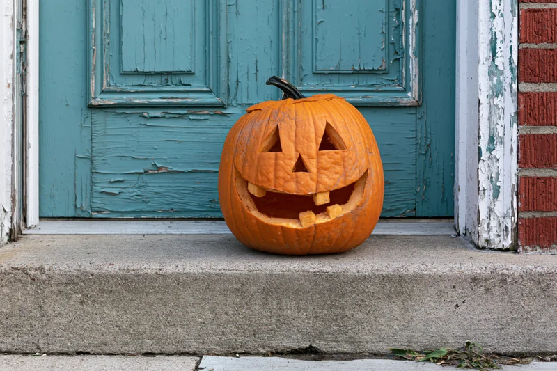 Carved pumpkin with toothy grin on concrete step in front of teal door