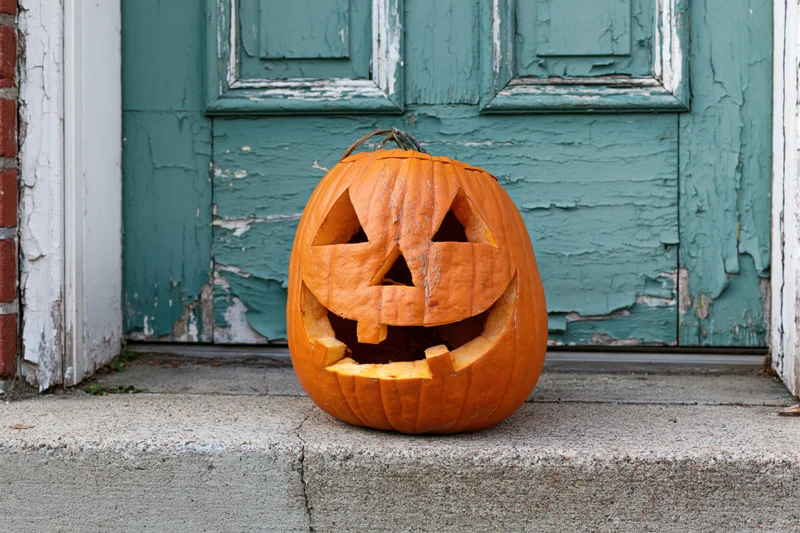 Carved pumpkin with toothy grin on concrete step in front of weathered teal door