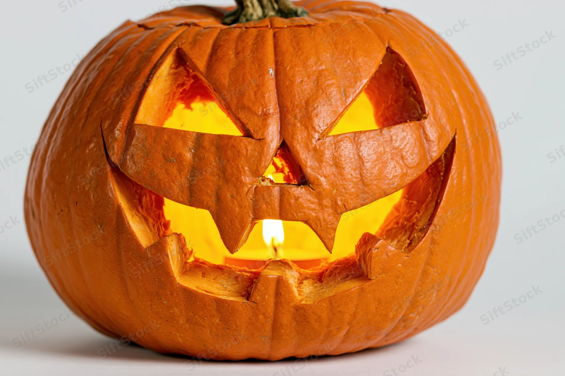 Carved pumpkin with jagged grin lit from within on white background