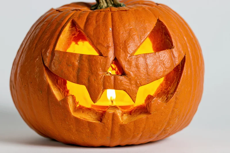Carved pumpkin with jagged grin lit from within on white background