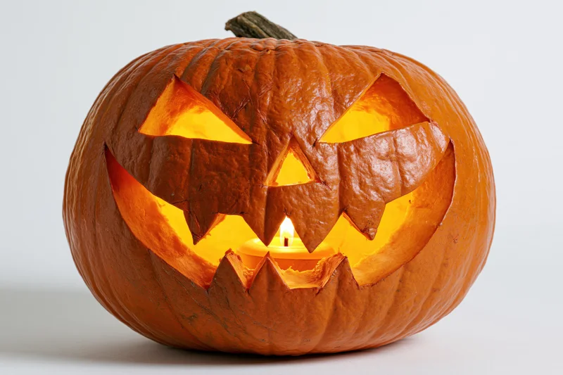 Carved pumpkin with jagged grin and glowing eyes lit from within on white background