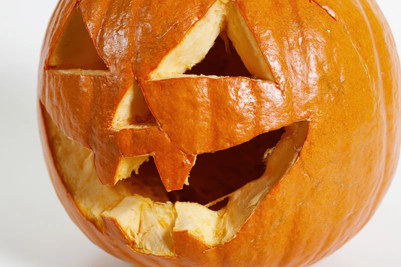 Carved pumpkin with jagged triangular eyes and wide mouth on white background