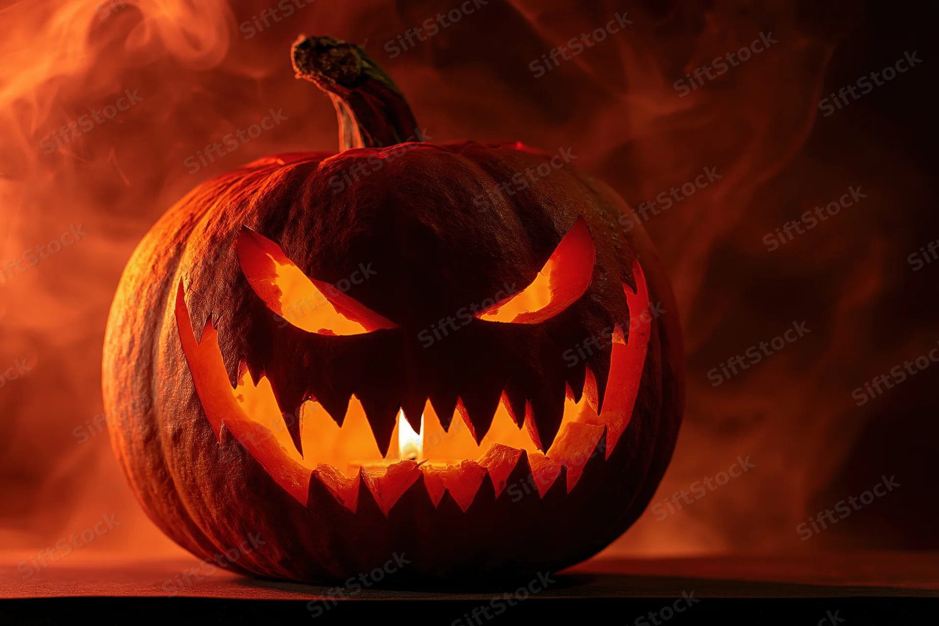 Carved pumpkin with jagged face glowing from within, surrounded by smoke in dark setting
