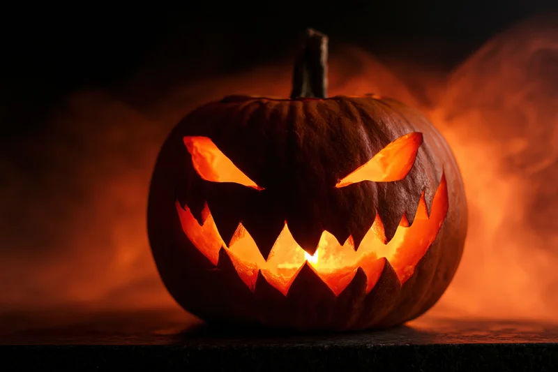 Carved pumpkin with jagged face glowing in dark smoke-filled setting