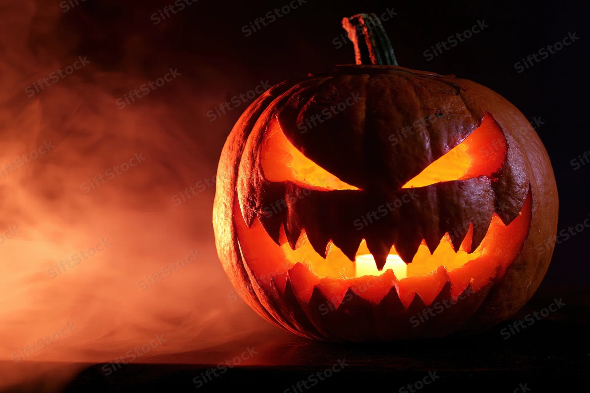 Carved pumpkin with jagged face glowing in the dark surrounded by smoke
