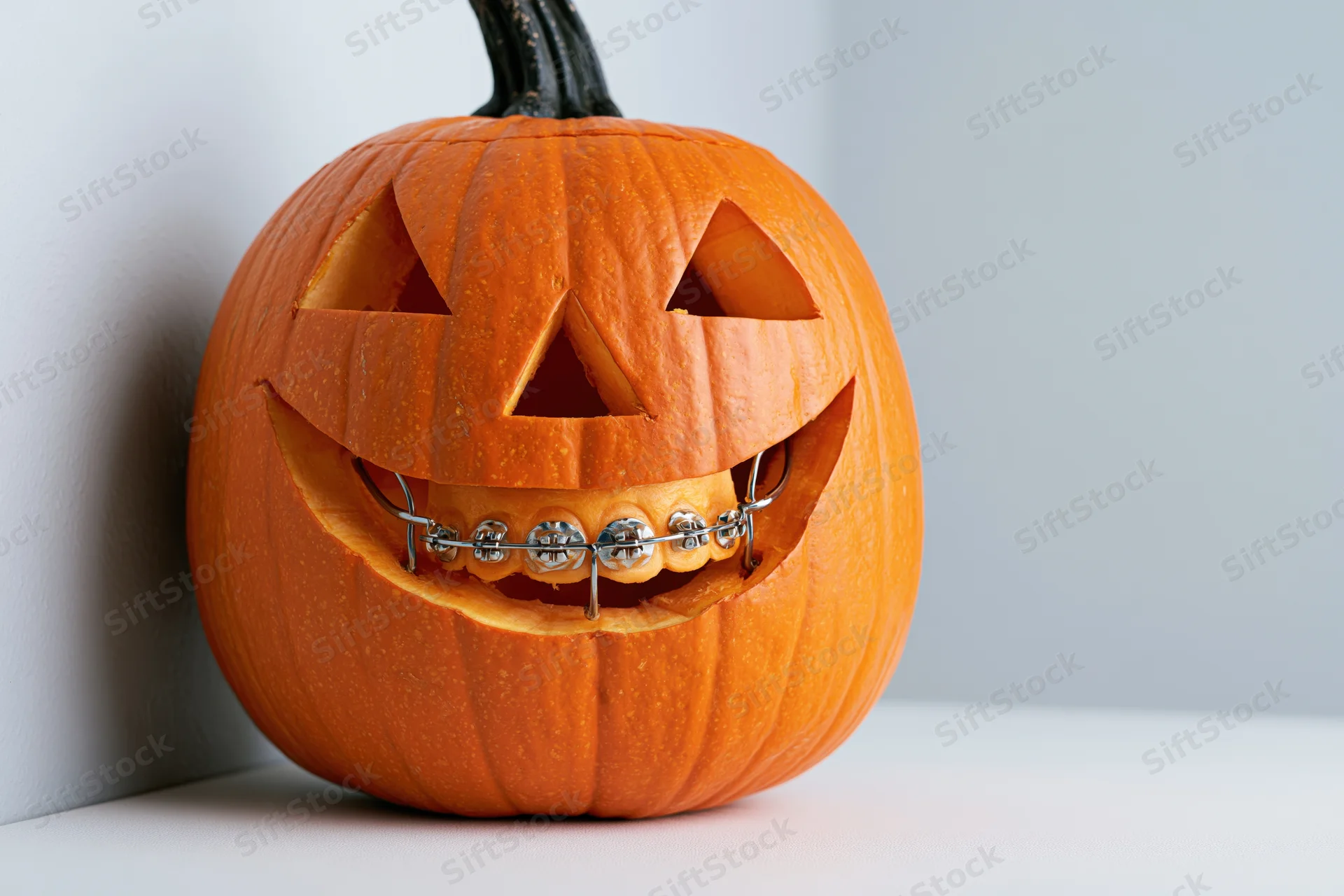 Carved pumpkin with dental braces in a corner against a white wall