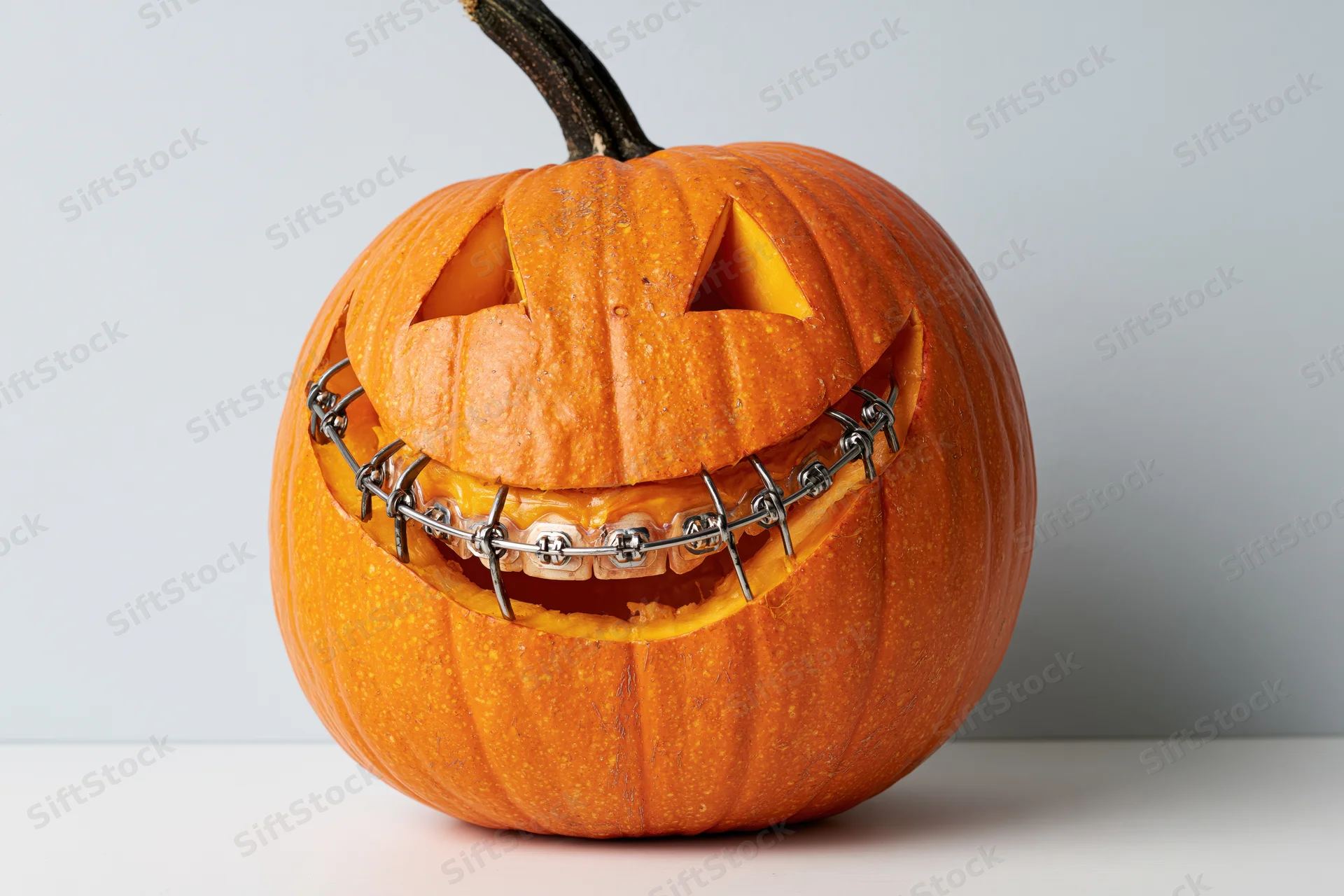 Carved pumpkin with dental braces on its mouth, isolated on white background