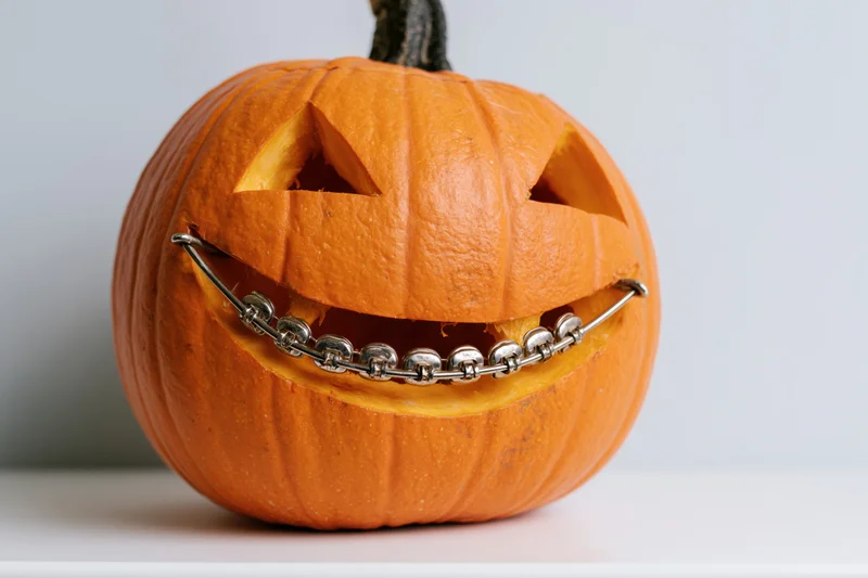 Carved pumpkin with metal dental braces on white surface for halloween decoration
