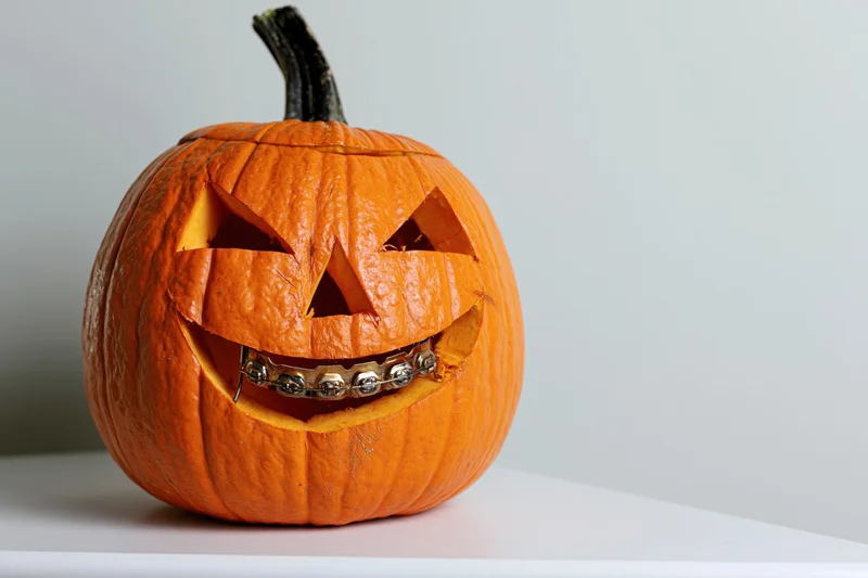 Carved pumpkin with dental braces on its mouth on a white surface